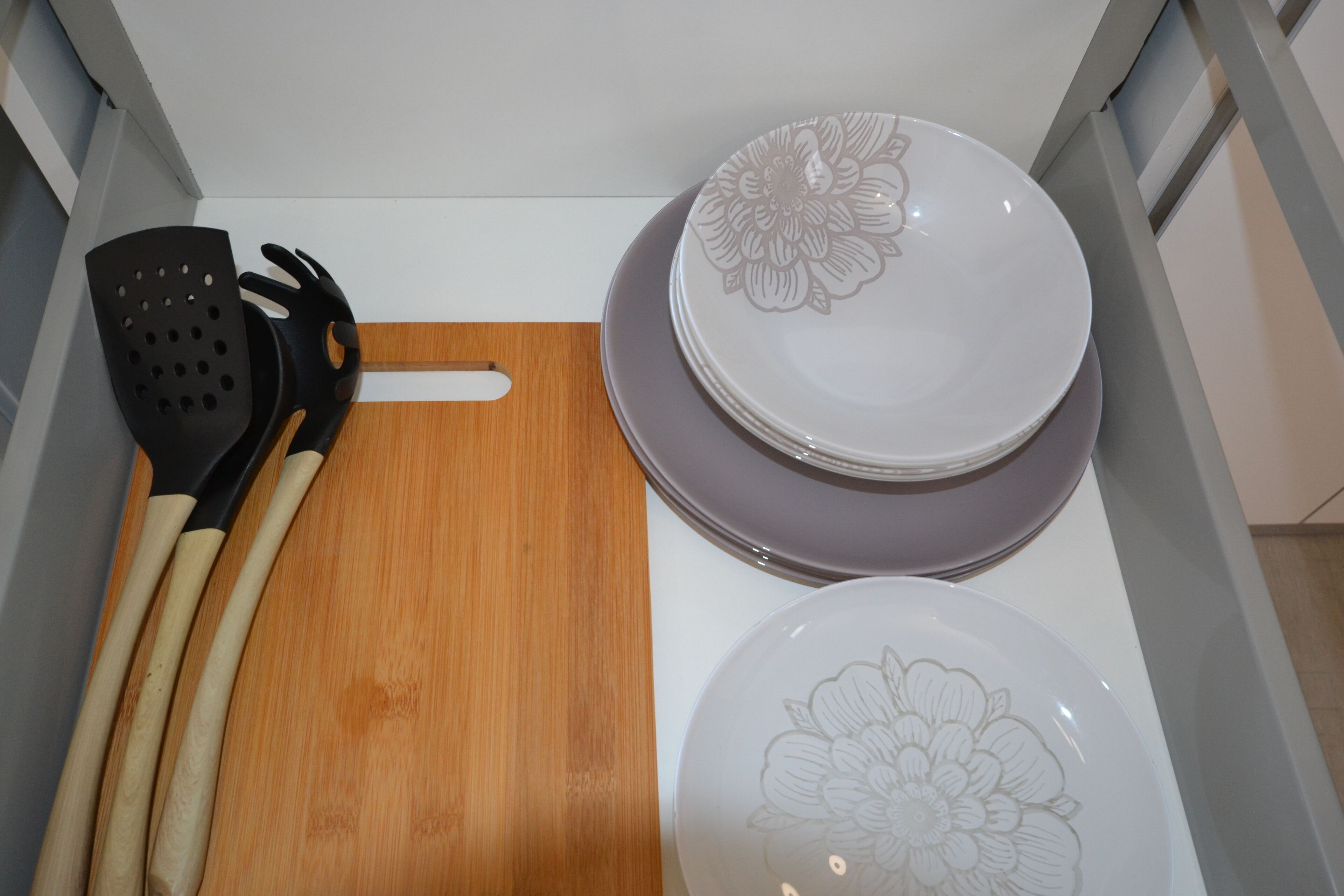 Un coin cuisine avec une planche à découper en bois, une spatule noire et deux assiettes superposées ornées de motifs floraux.
