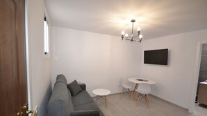 A modern living room with a grey sofa, a small round table, and a TV mounted on the wall.