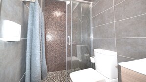 A modern bathroom with a glass-enclosed shower, a toilet, and a sink.