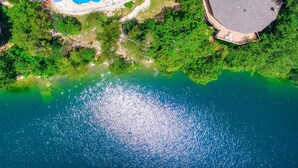An aerial view of a coastal area with a swimming pool, a covered structure, and dense greenery. - The Treehouse on Lake Travis (Lakeway)