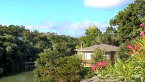 A house with a deck overlooking a lake, surrounded by dense greenery. - The Treehouse on Lake Travis (Lakeway)
