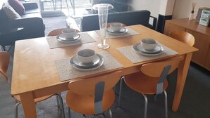 Uma área de refeições com uma mesa de madeira posta para quatro pessoas, rodeada por cadeiras laranja.