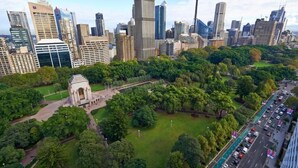 Vista aérea de um horizonte urbano com uma mistura de edifícios modernos e históricos, uma torre imponente e uma grande área de parque verde.