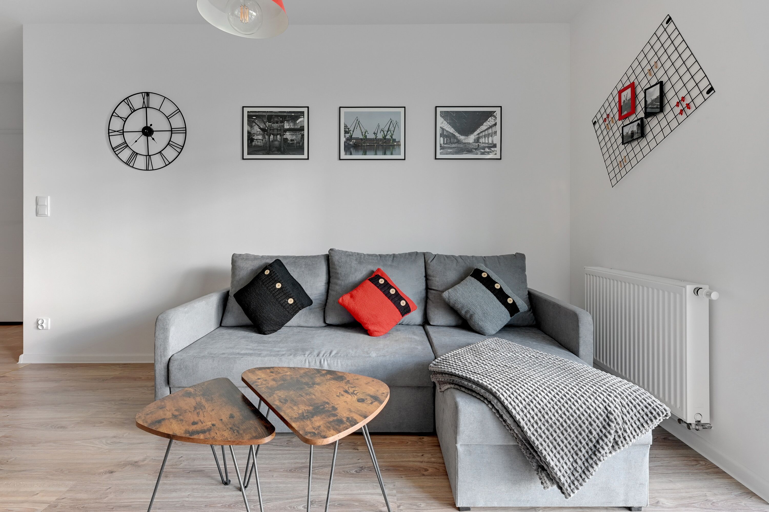 A modern living room with a grey sofa, two wooden side tables, and a black clock on the wall.
