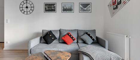 A modern living room with a grey sofa, two wooden side tables, and a black clock on the wall.
