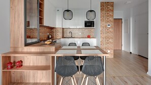Una cocina moderna con salpicadero de ladrillo, armarios blancos y un microondas. Hay un comedor con una mesa de madera y sillas negras.