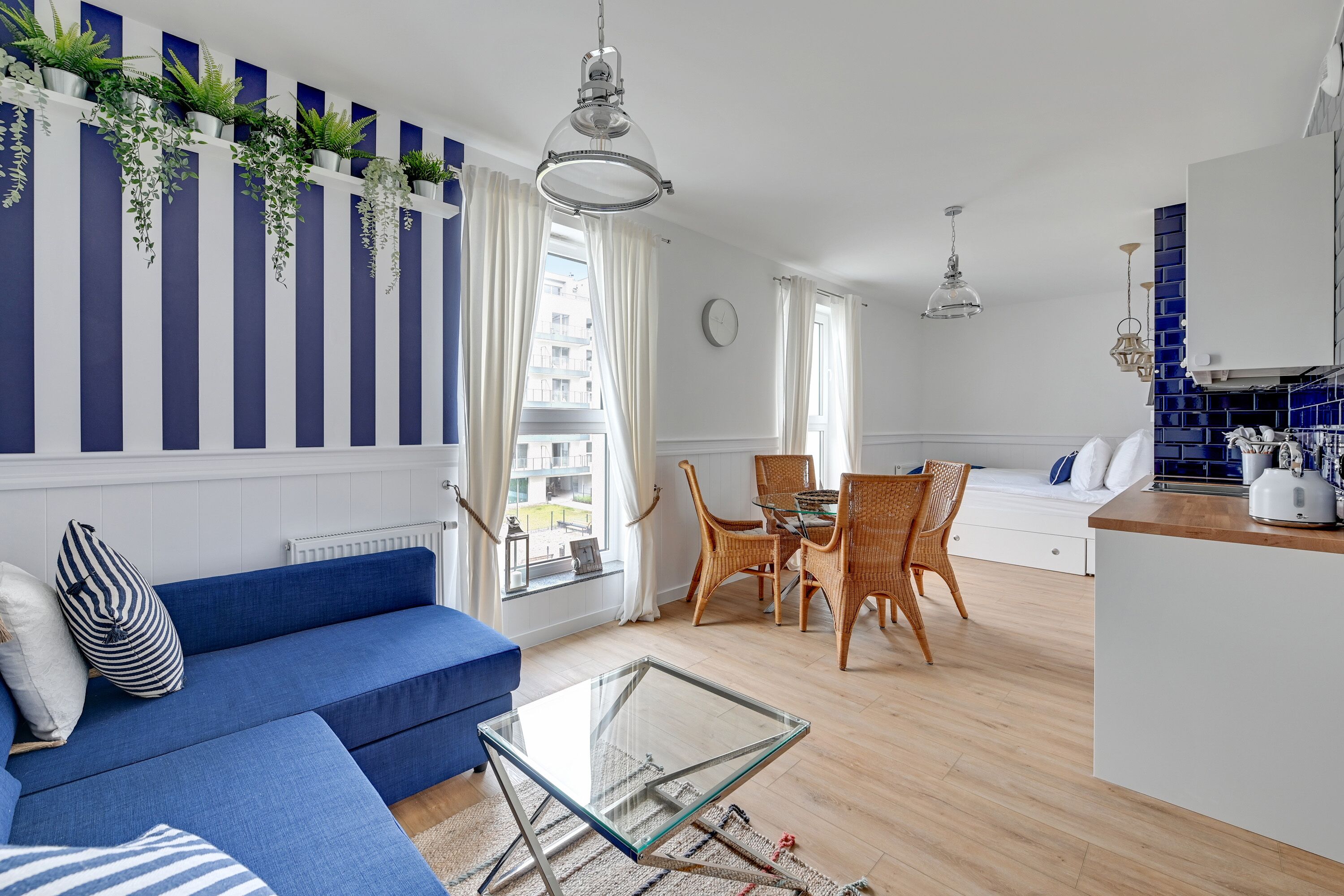 A modern living room with a blue sofa, glass coffee table, and a dining area with wicker chairs.