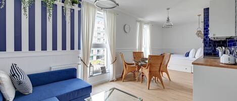 A modern living room with a blue sofa, glass coffee table, and a dining area with wicker chairs.