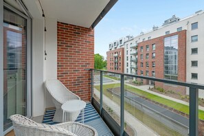 A balcony with wicker chairs and a table, overlooking a street and buildings. - NORDBYHUS Apartamenty Angielska Grobla (Gdansk)