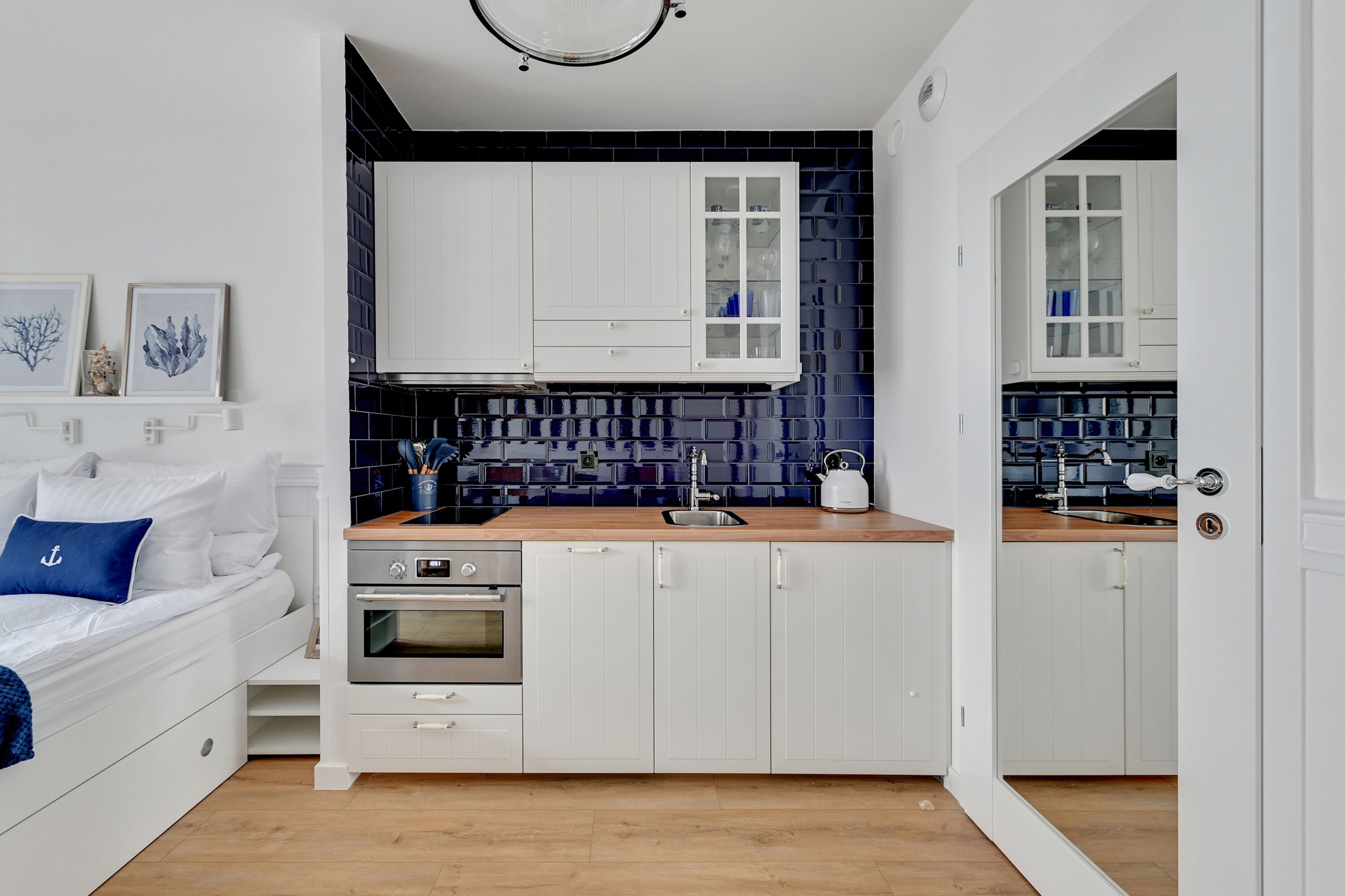 Et lille køkken med hvide skabe, en træbordplade og en backsplash med blå fliser.