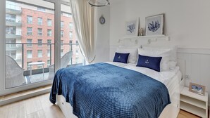 Un dormitorio con una cama grande, vista de un edificio de ladrillo rojo, un reloj de pared blanco y dos cuadros enmarcados.