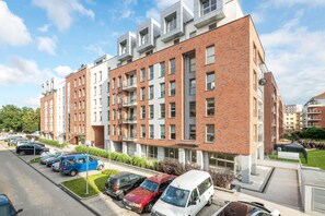 A multi-story residential building with a brick facade, balconies, and a parking lot with various cars. - NORDBYHUS Apartamenty Angielska Grobla (Gdansk)