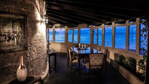 A dining area with a view of the sea, stone walls, and a table set with glasses. - Windmill Tower Beach House in Rhodes island (Ialisos)