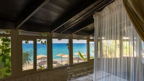 A room with a bed, a view of the beach, and a balcony with umbrellas. - Windmill Tower Beach House in Rhodes island (Ialisos)
