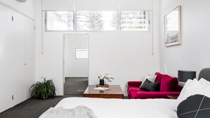 Una habitación de hotel moderna con una cama grande, un sofá rojo, una mesita de centro y vistas a árboles a través de las ventanas.
