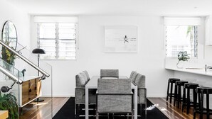 Una cocina moderna con comedor, que cuenta con una isla central, sillas tapizadas en gris y un amplio ventanal con persianas.