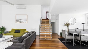 Una sala de estar moderna con una escalera, un sofá verde, un sofá gris y un comedor con sillas y una mesa.