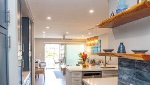 A modern kitchen with white cabinetry, a marble countertop, and a dining area with a view to the outside.