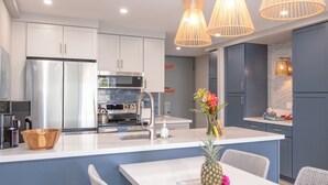 A modern kitchen with white cabinets, stainless steel appliances, a central island with seating, and pendant lighting.