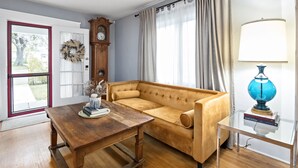 A living room with a wooden table, a sofa, a clock, and a lamp.