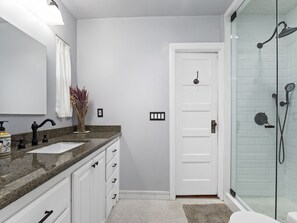 Baño con encimera de granito, puerta blanca y cabina de ducha de vidrio.