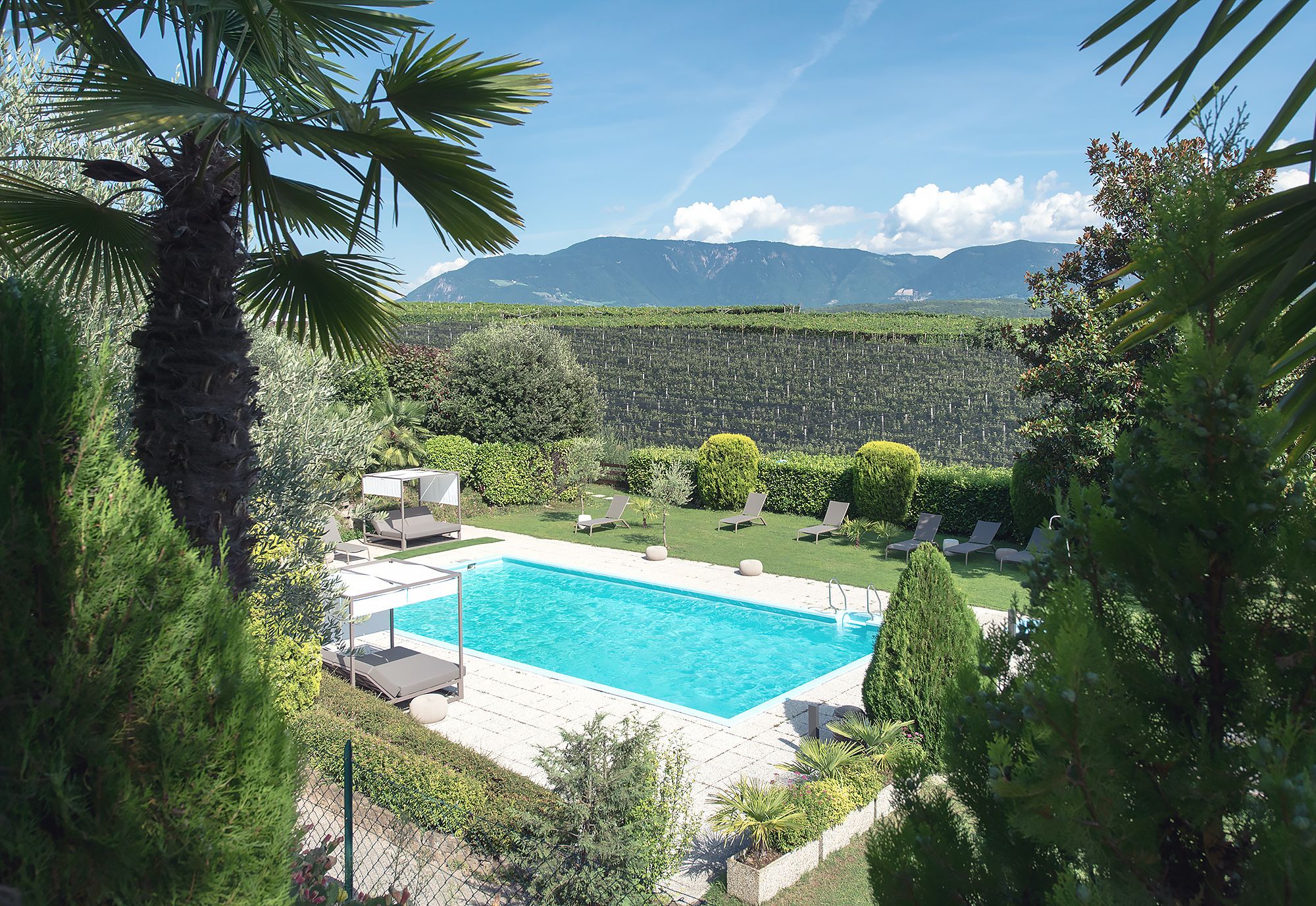 A swimming pool with lounge chairs, surrounded by greenery and mountains in the background.