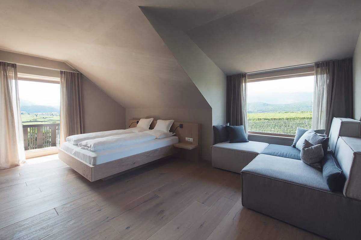 A bedroom with a bed, a sofa, and large windows offering a view of the outdoors.
