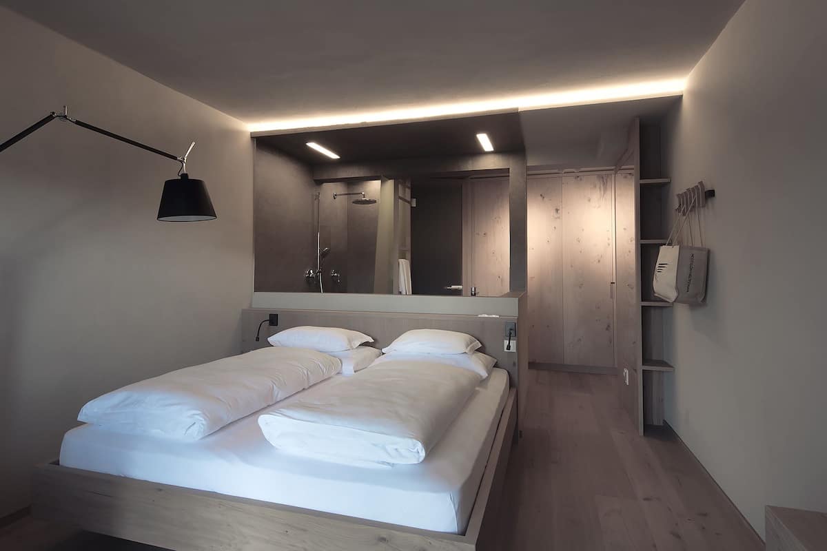 A modern bedroom with a wooden bed, a large mirror, and a bedside lamp.