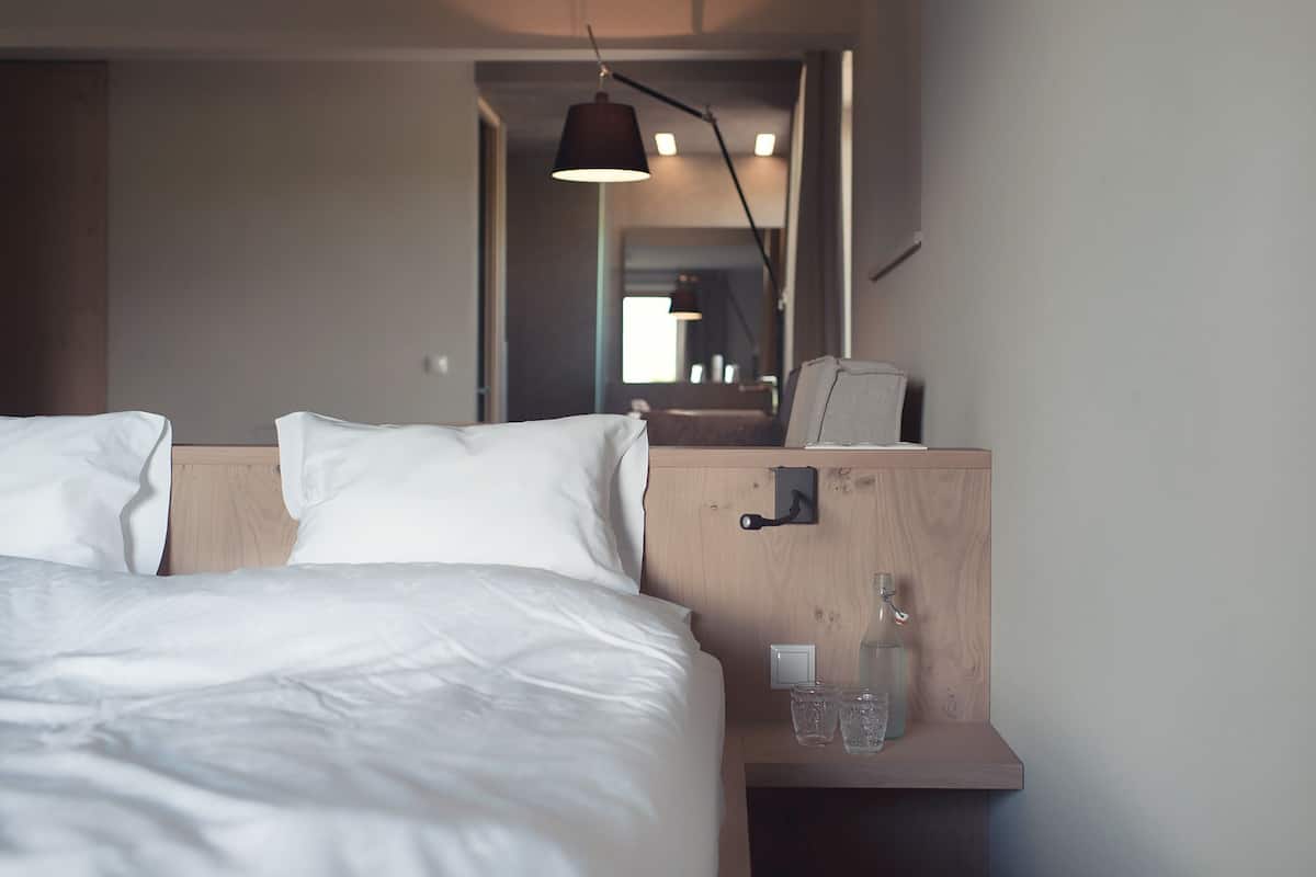 A hotel room with a bed, bedside table, and a mirror.