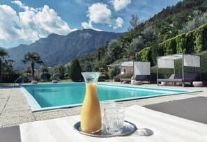 A poolside setting with a clear view of mountains, a lounge area, and a table with a drink and glass. - Das Wanda (Caldaro Sulla Strada del Vino)