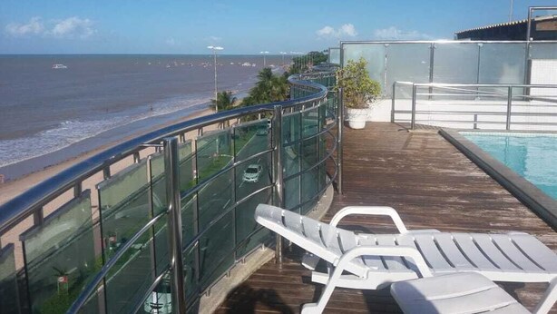 Eine Terrasse mit Glasgeländer mit Blick auf Strand und Pool.