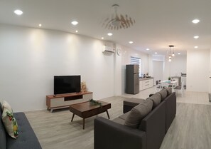 Una sala de estar moderna con televisor de pantalla plana, sofá, mesa de centro y un comedor con mesa y sillas.