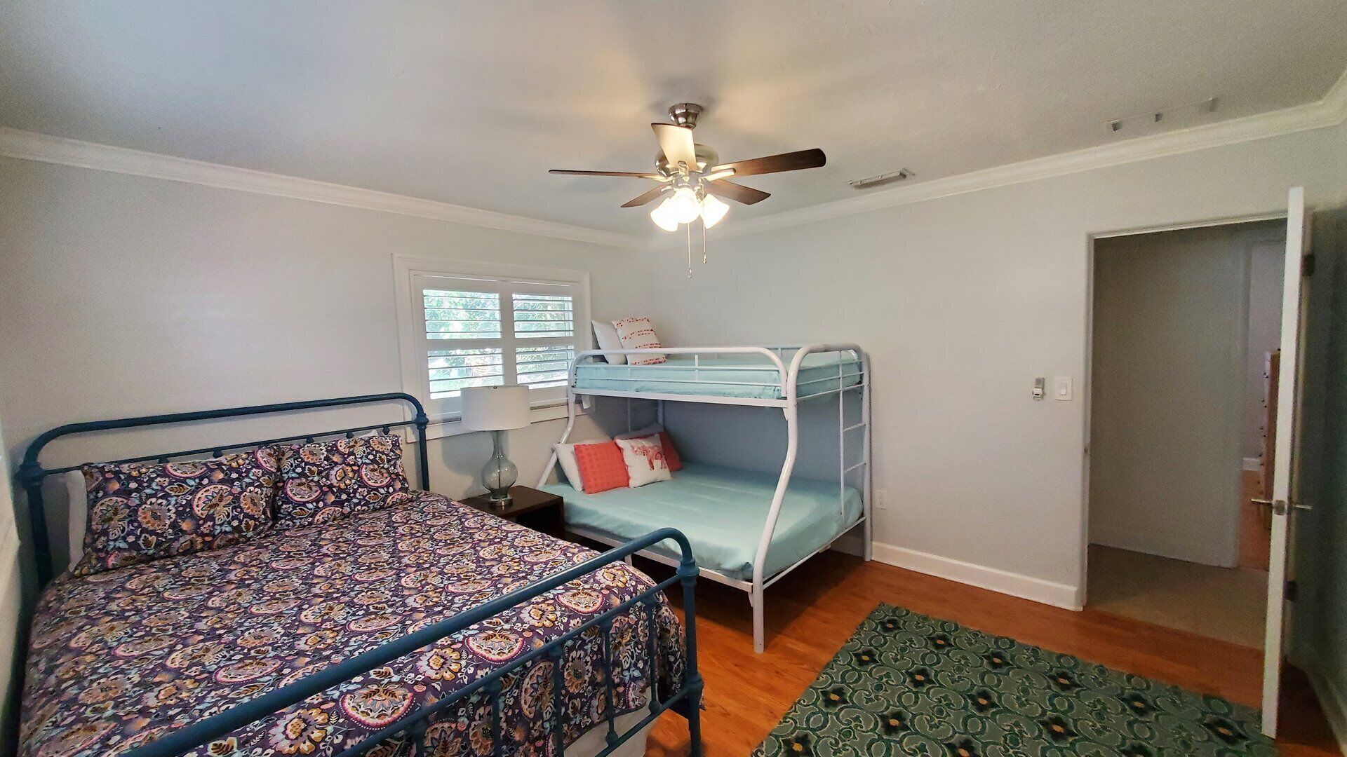 A bedroom with a bunk bed, a single bed, a ceiling fan, a window with blinds, and a door.