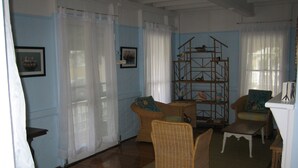 Quarto com piso de madeira, móveis de vime e uma estante de madeira.