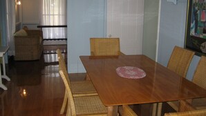 Uma área de refeições com mesa de madeira e cadeiras de vime, uma cesta de vime e uma porta branca.