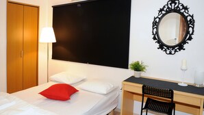 Ein Hotelzimmer mit Bett, Schreibtisch, Stuhl, Spiegel, Lampe und einer Zimmerpflanze.