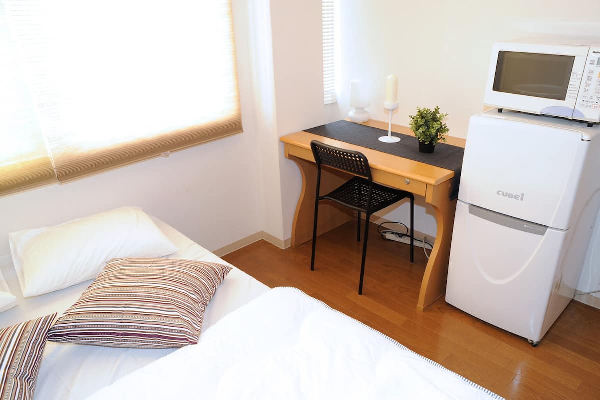 A hotel room with a bed, a desk, a chair, a microwave, and a refrigerator.