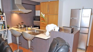 Eine moderne Küche mit Kochinsel, Barhocker, Backofen und Kühlschrank.