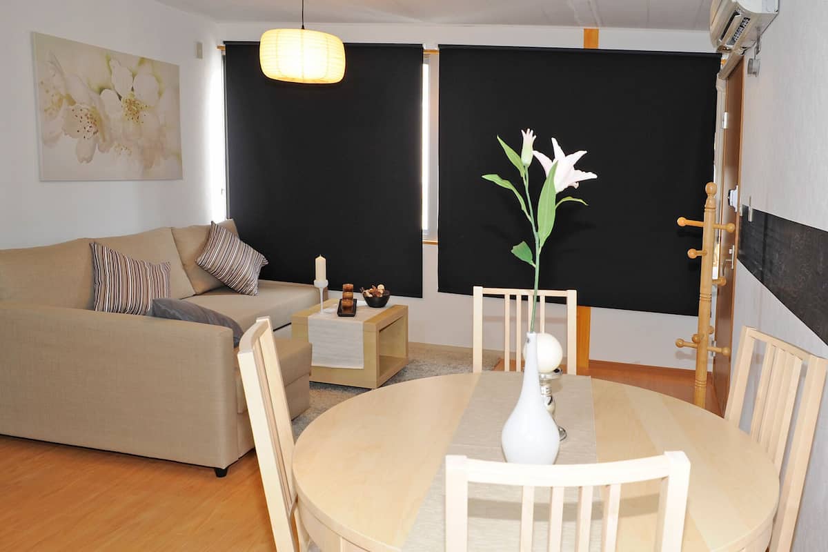 A modern living room with a beige sofa, a round wooden dining table, and a white vase with flowers.