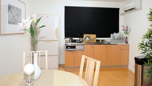 Eine kleine Küche mit Kühlschrank, Herd und Spüle. Ein Esstisch mit Stühlen und eine Blumenvase sind ebenfalls vorhanden.