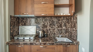 A compact kitchen with wooden cabinets, a gas stove, a sink, and a marble backsplash. - Hotel Cosmos (Batumi)