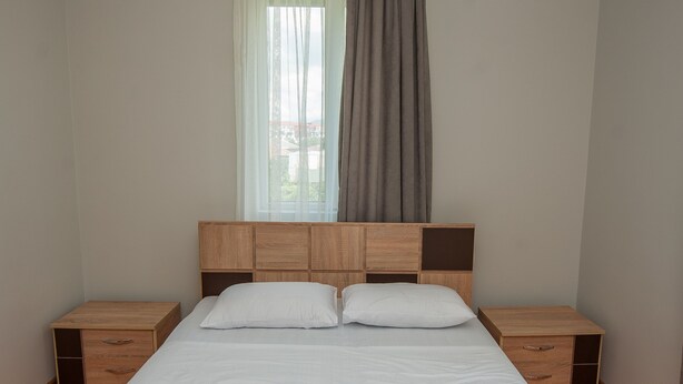 A neatly made bed with white linens and towels, a wooden headboard, bedside tables, and a hanging lamp. - Hotel Cosmos (Batumi)