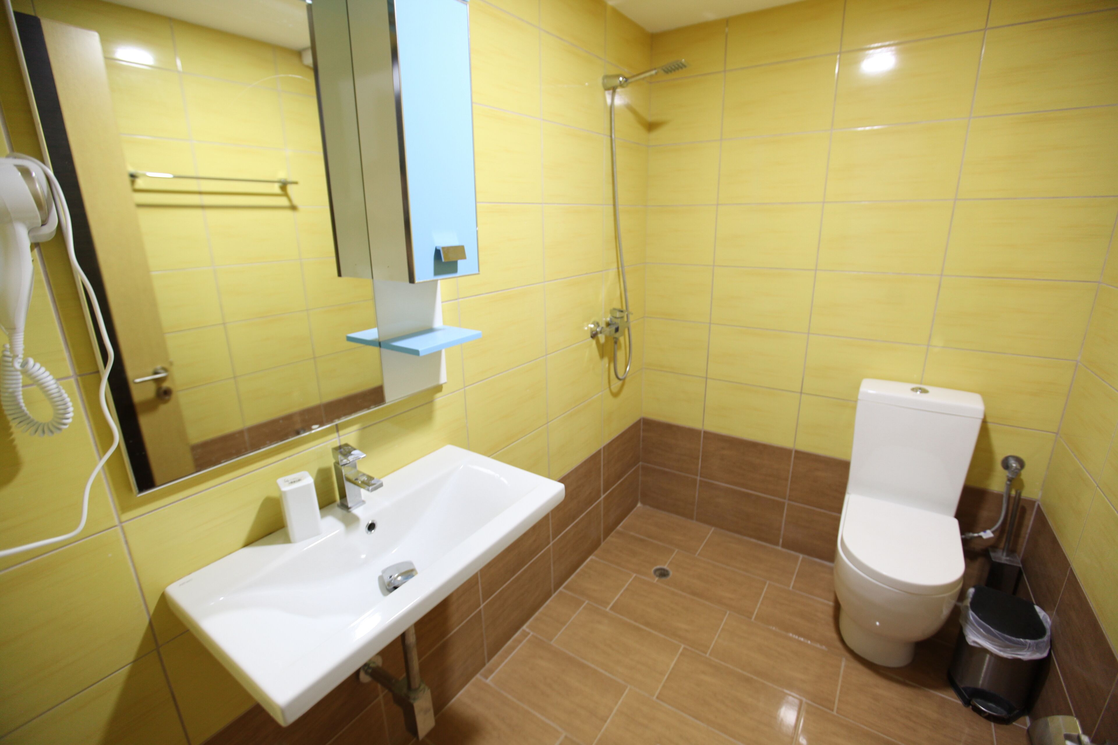 A bathroom with yellow tiles, a white sink, a toilet, and a shower.