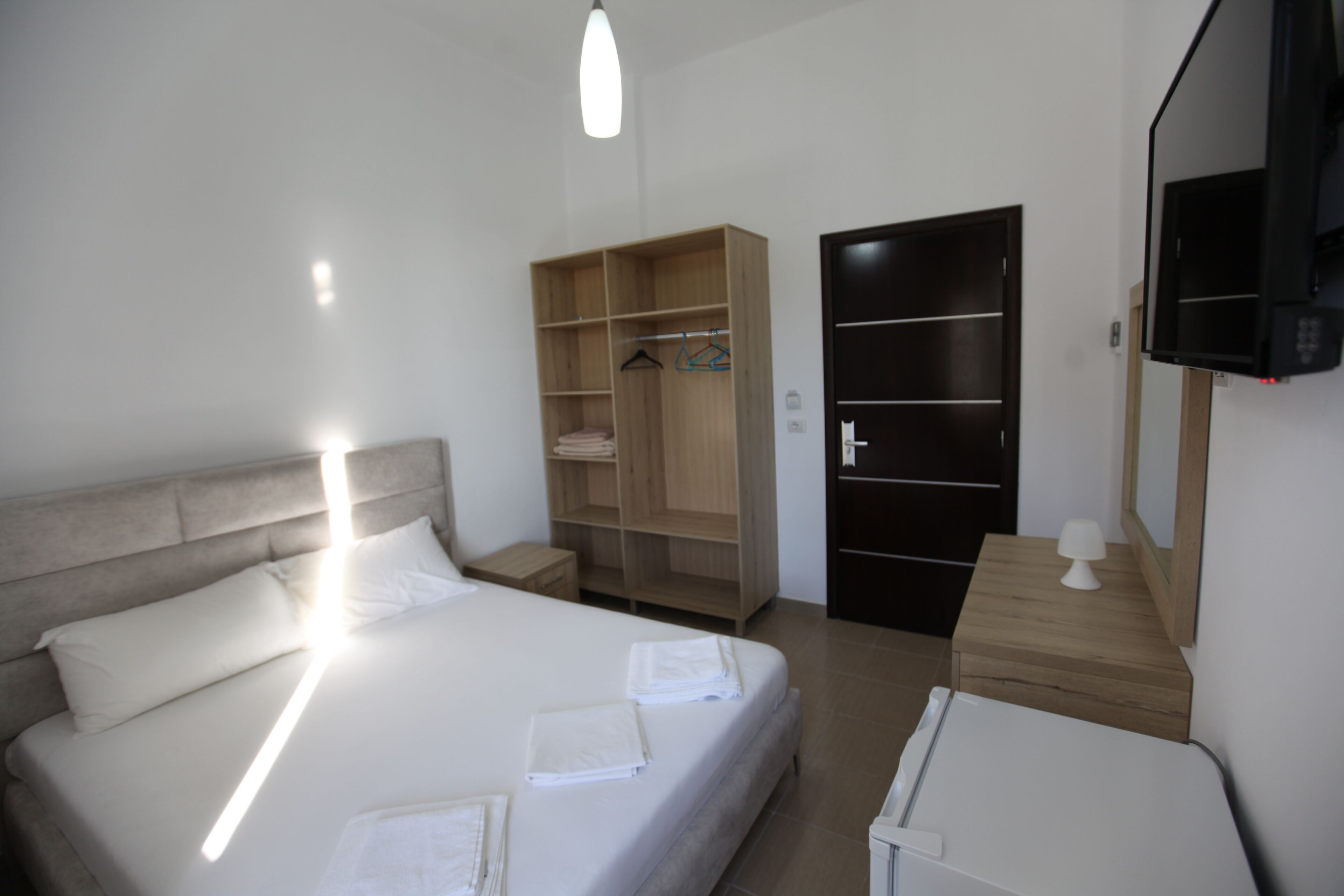 A bedroom with a bed, a wooden wardrobe, a TV, and a small table.