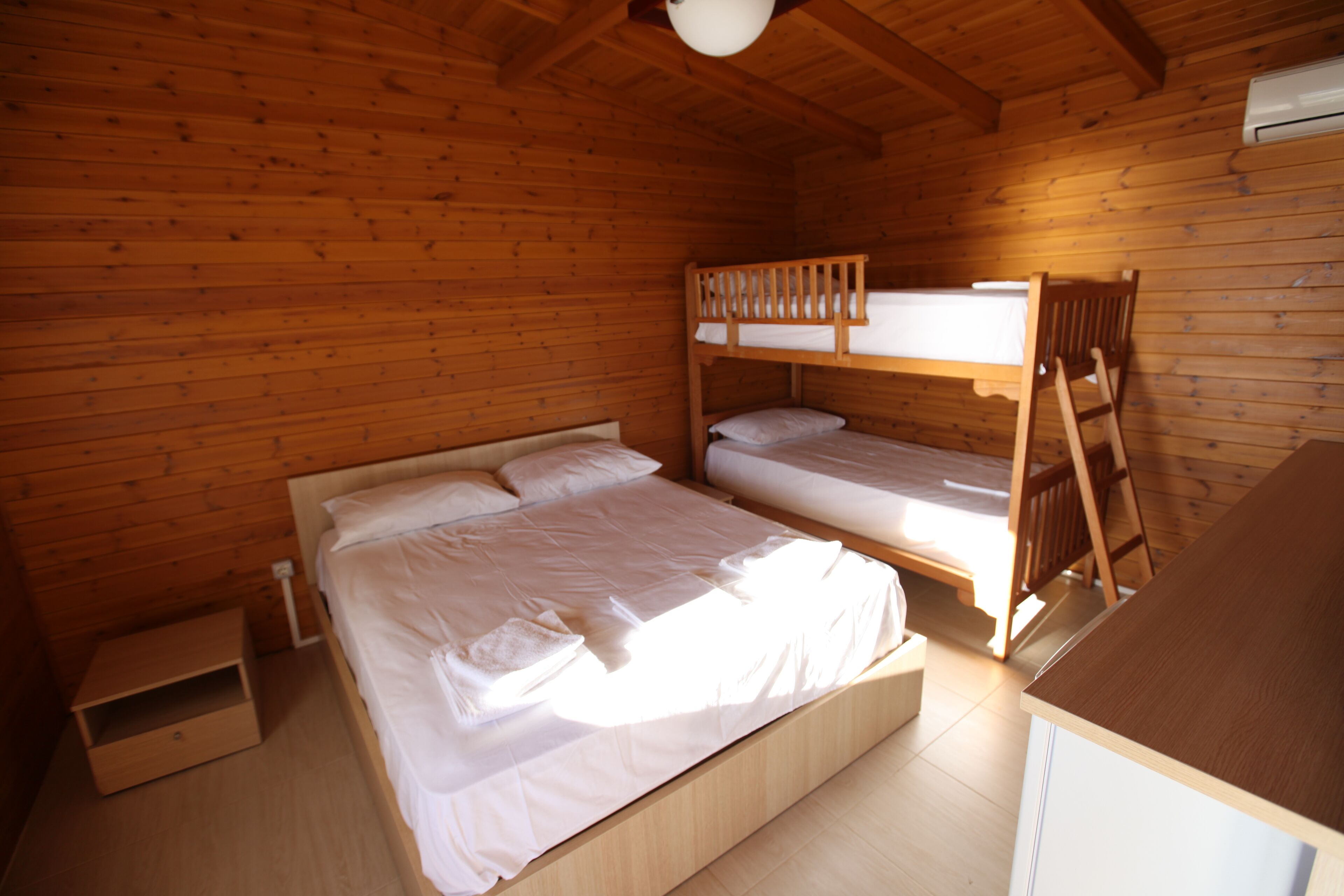 A wooden cabin room with a bunk bed, a single bed, a small wooden cabinet, and a ladder.