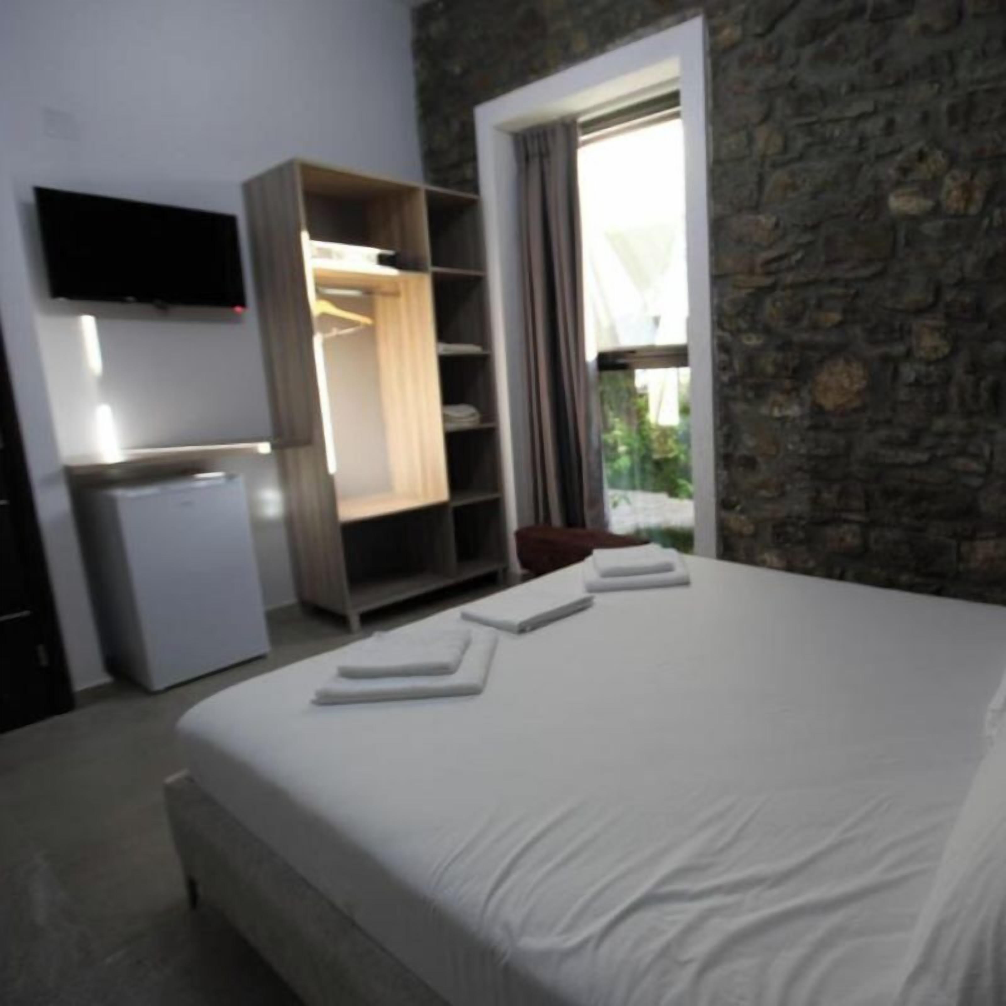 A bedroom with a bed, a wardrobe, a television, and a window with curtains.