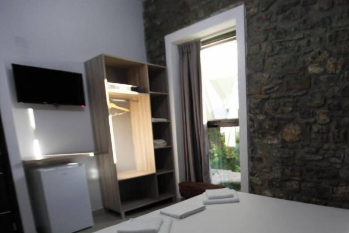 A bedroom with a bed, a wardrobe, a television, and a window with curtains.