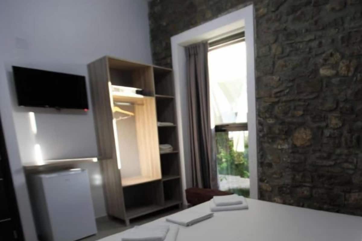 A bedroom with a bed, a wardrobe, a television, and a window with curtains.