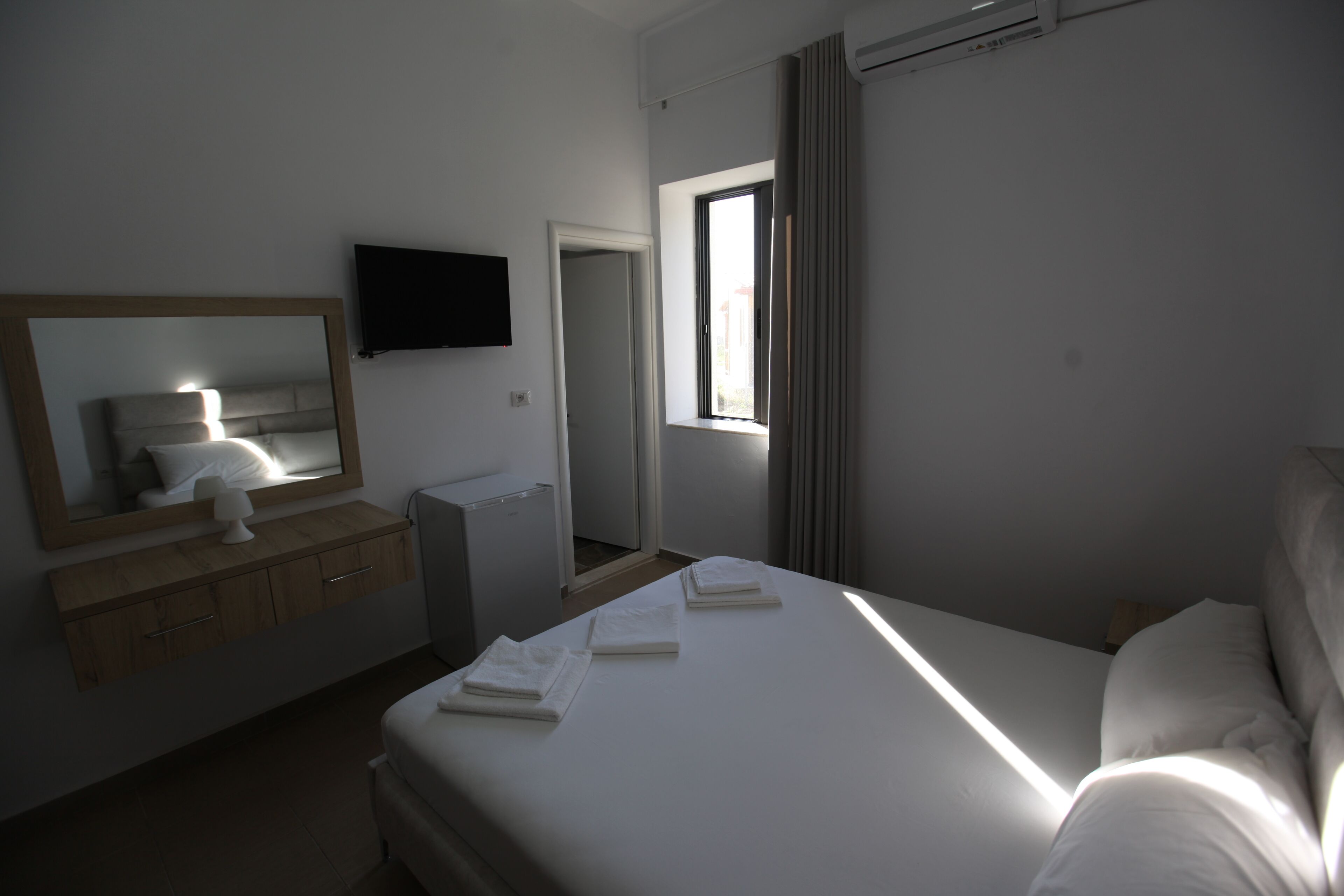Une chambre d’hôtel avec un lit, une table de chevet, un miroir, une télévision et une fenêtre avec des rideaux.