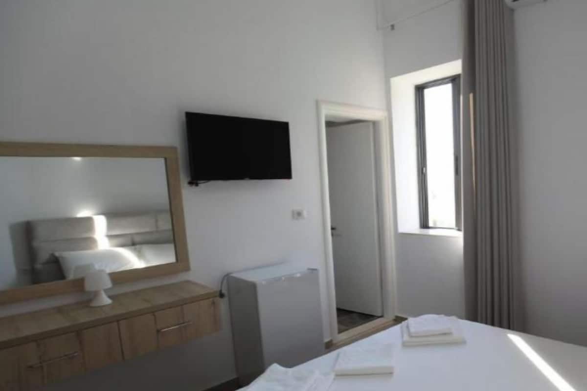 A hotel room with a bed, a TV mounted on the wall, a bedside table, and a window.